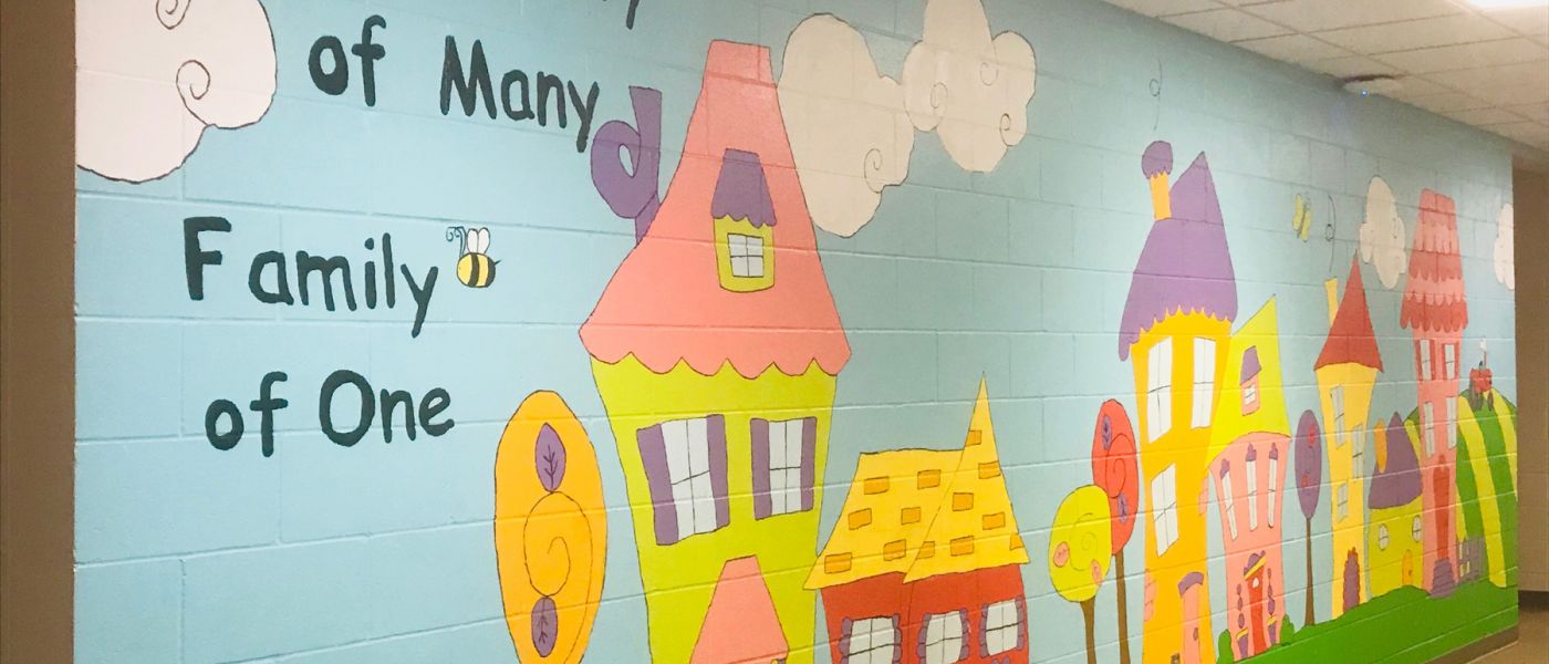 Painted mural for colorful homes that reads "Community of many, family of one"