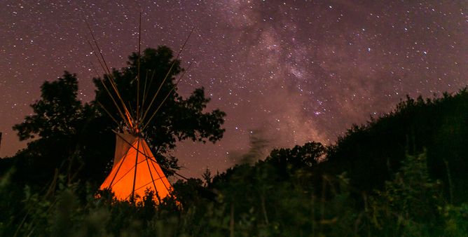 a teepee aglow at night with constellations in clear view