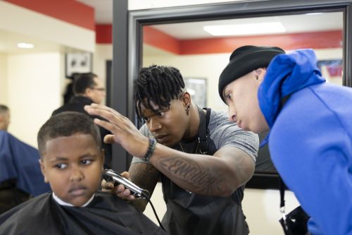 barber shows student how to user trimmers on boy's head