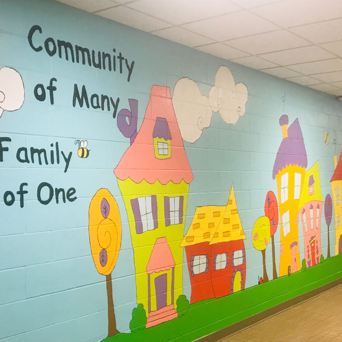 Painted mural for colorful homes that reads "Community of many, family of one"