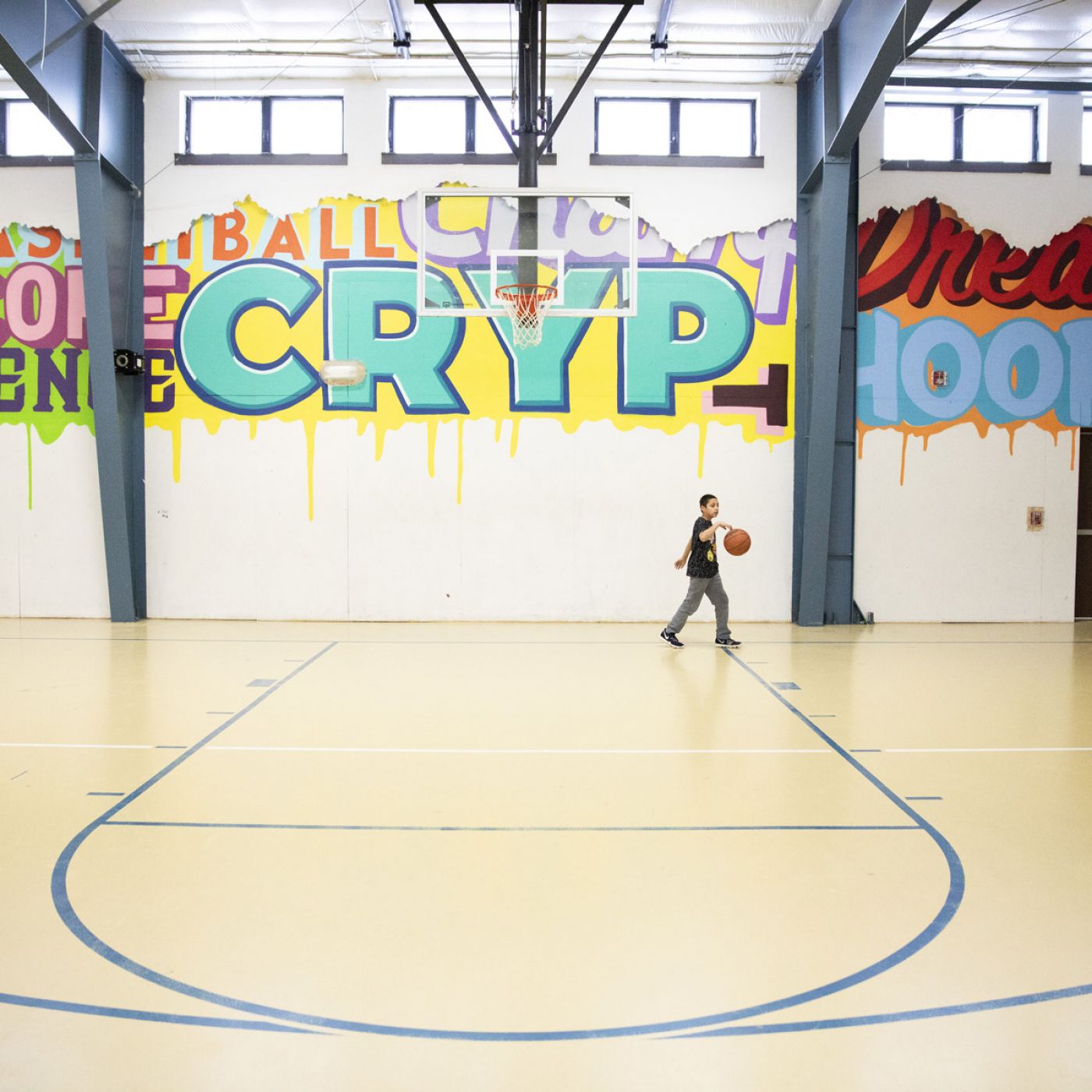 Boy bouncing basketball in a gym with colorful, expressive graffiti on walls